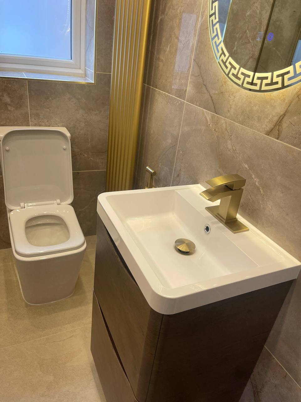 Brushed gold square basin tap installation in a marble cloakroom in South West London